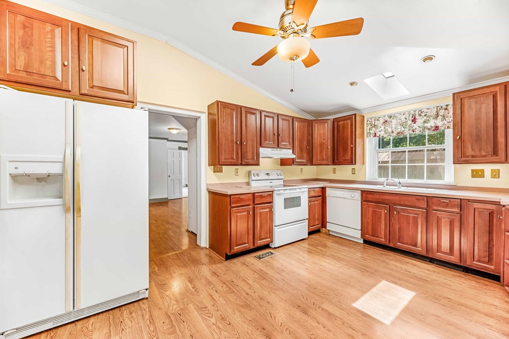 a kitchen with wooden cabinets and white appliances and a ceiling fan