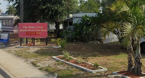 A sign for Pine Ridge Court Mobile Homes For Rent stands in front of a house.