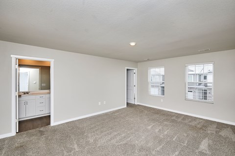 A spacious empty room with a carpeted floor and a doorway leading to another room.