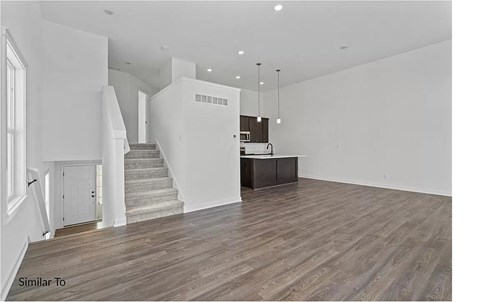 A spacious room with wooden flooring and a staircase leading to another level.