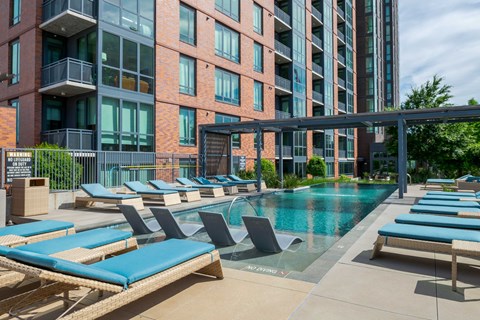 A pool area with sun loungers and a building in the background.