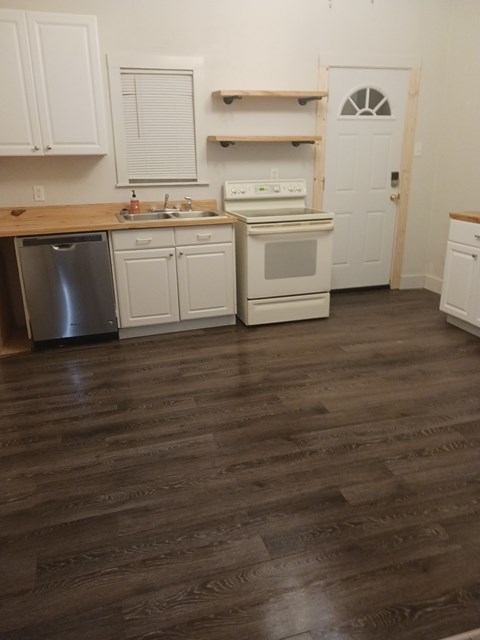 A kitchen with white cabinets and a wooden floor.
