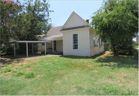 A white house with a porch and a tree in front.
