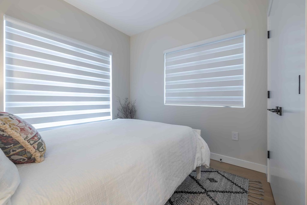 A bedroom with a bed, pillow, and a window with blinds.