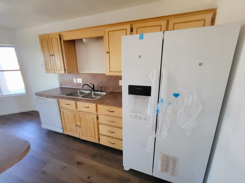 an empty kitchen with a refrigerator and wooden cabinets