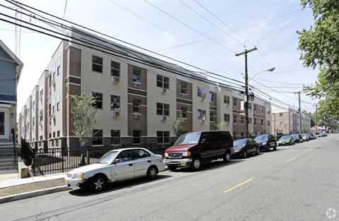 A street view of a residential area with cars parked on the side of the road and apartment buildings in the background.