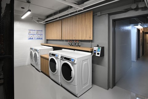 Three front loading washing machines are lined up in a laundry room.
