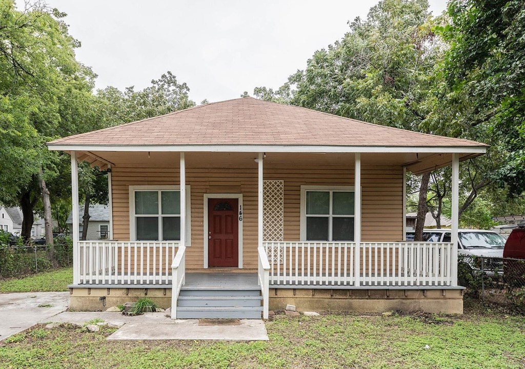 a small brown house with a porch and a red door