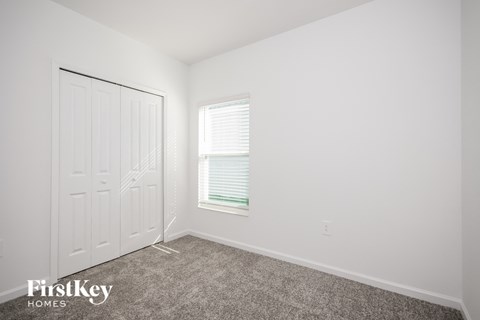 a bedroom with white walls and carpet and a white door and window