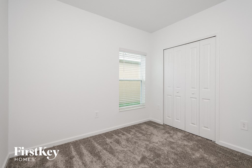 a bedroom with white walls and carpet and a door to a closet