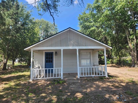 a small white house with a porch and trees around it