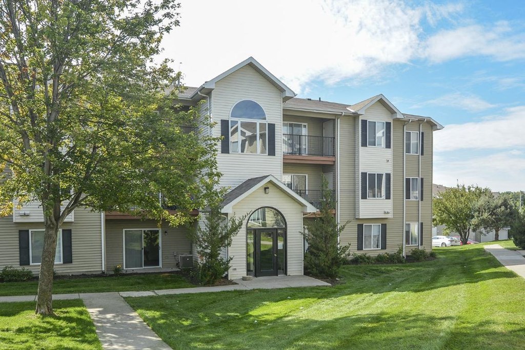 the front of an apartment building with a lawn and trees