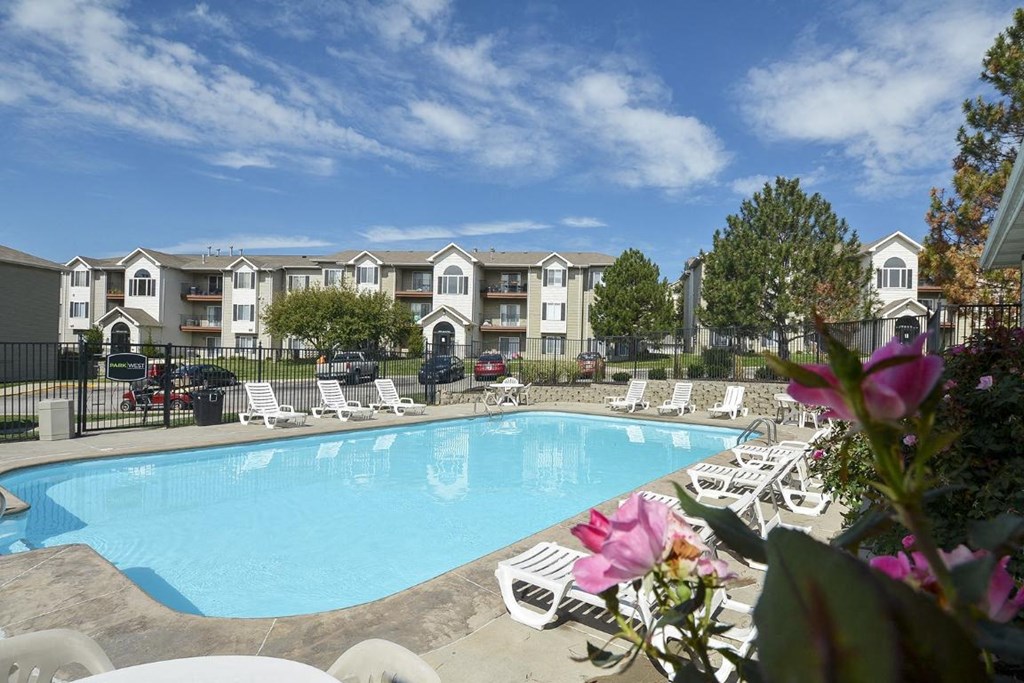 a swimming pool with white chairs and a building in the background