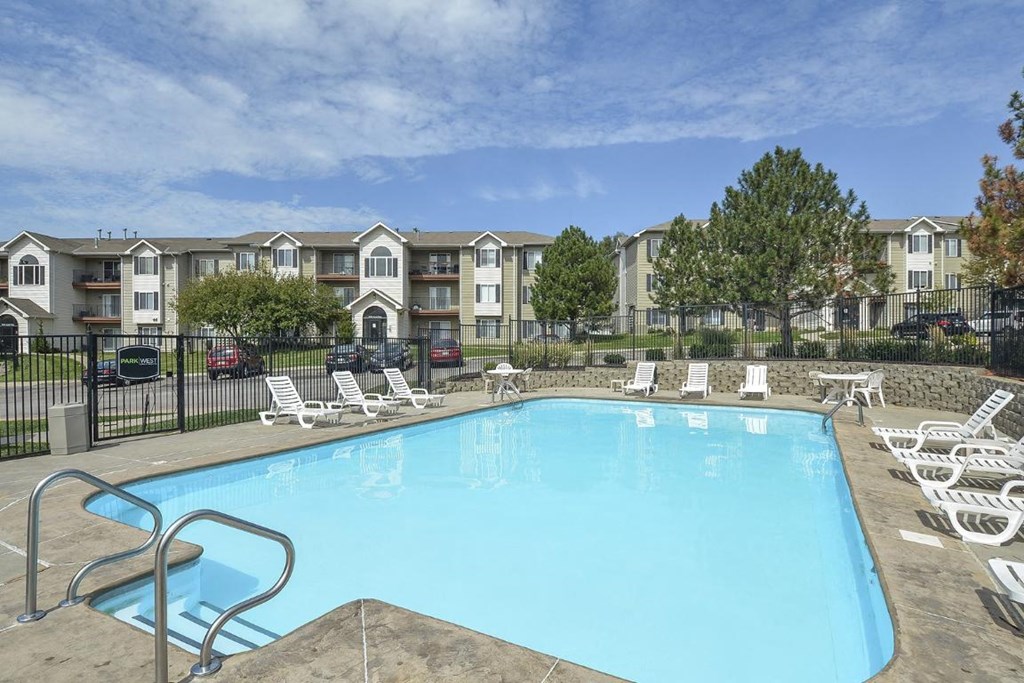 a swimming pool with white chairs in front of an apartment building