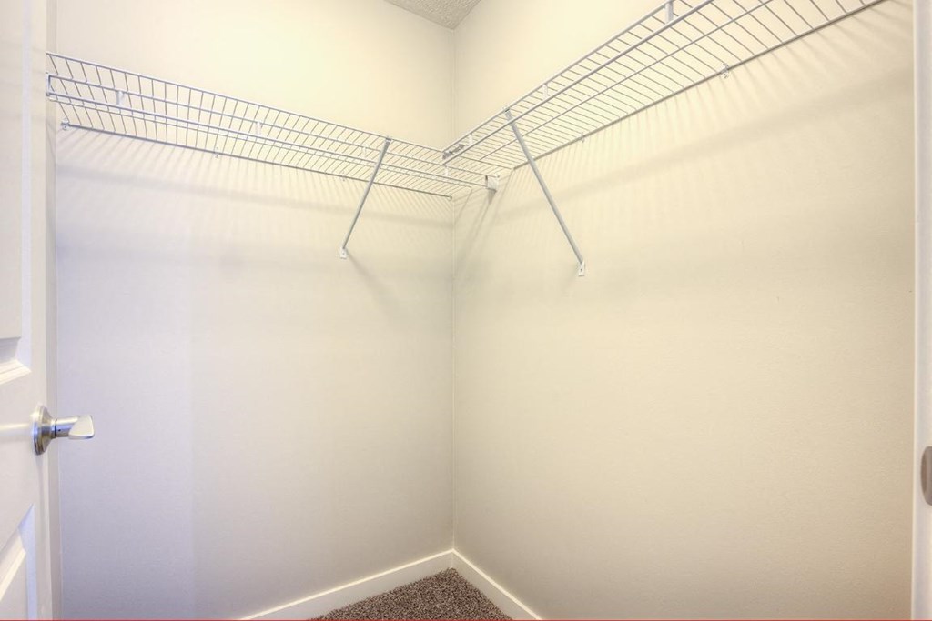 a white walk in closet with a wire shelf on the wall