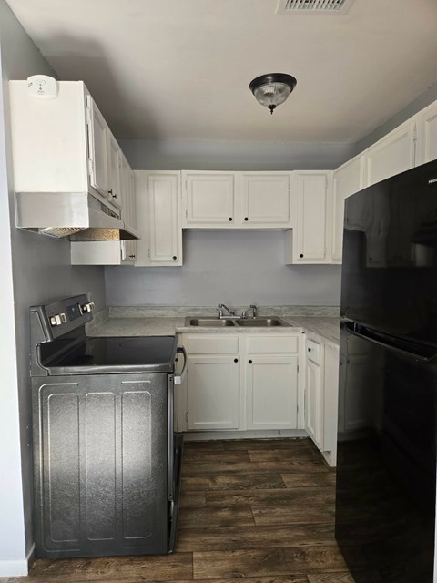 A kitchen with white cabinets and a black refrigerator.