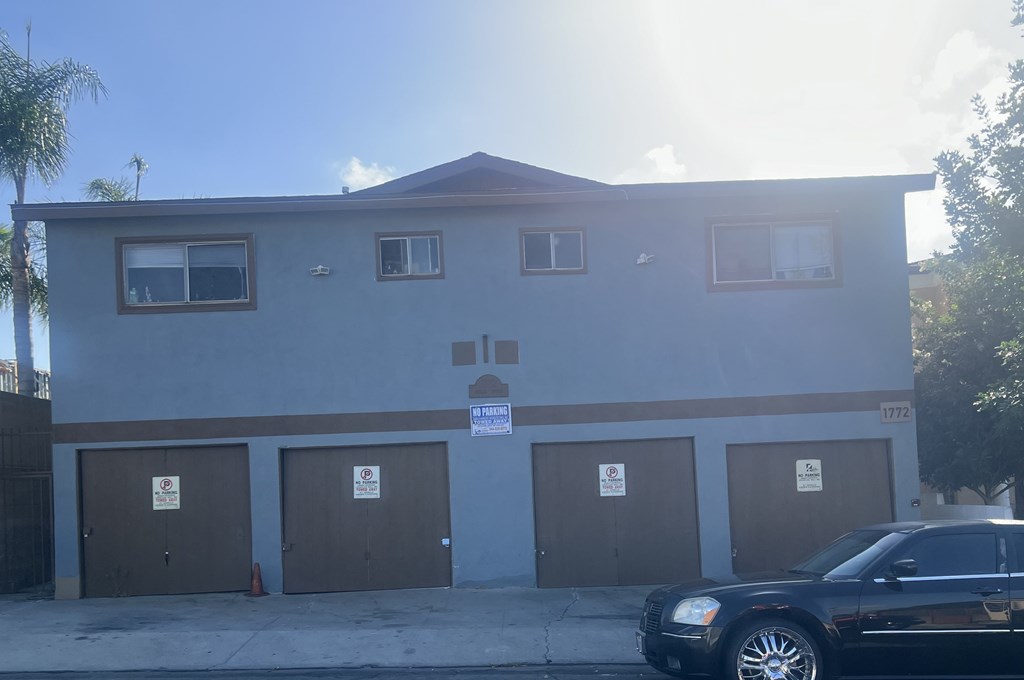 A black car is parked in front of a building with brown garage doors.