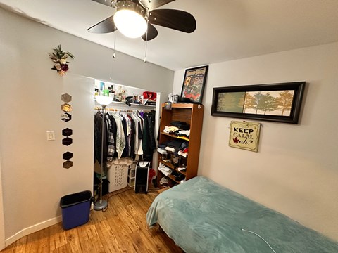 A bedroom with a bed, a fan, a wardrobe, and a picture frame on the wall.