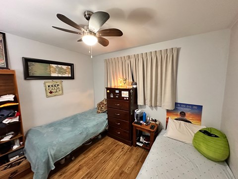 A bedroom with a bed, dresser, and a ceiling fan.
