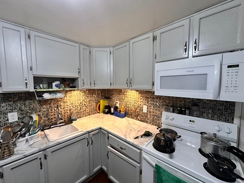 A kitchen with white cabinets and a white stove top oven.