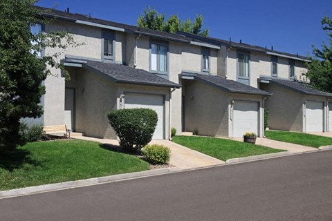 A row of houses with green lawns and trees in the background.