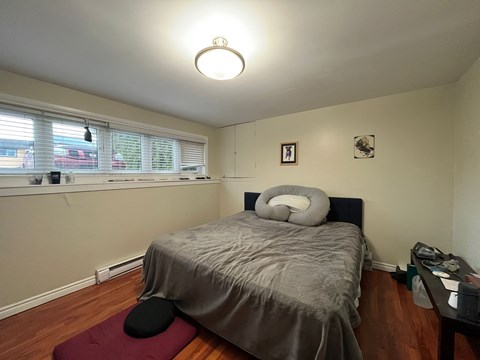 A bedroom with a bed, a desk, and a window with blinds.