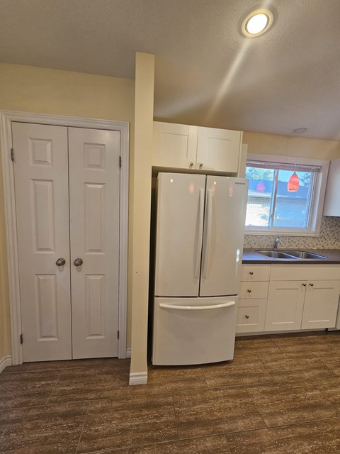 A white refrigerator in a kitchen with brown flooring.