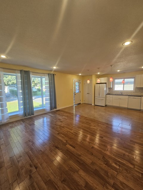 A room with wooden floors and a kitchen area in the background.