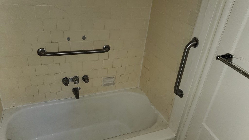 A white bathtub with a black grab bar mounted on the wall.