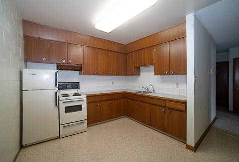 A kitchen with a white refrigerator and stove, brown cabinets, and a white counter.