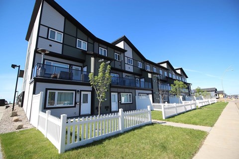 A white picket fence separates a row of modern townhouses.