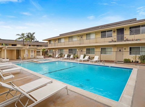 A swimming pool with sun loungers in front of apartment buildings.