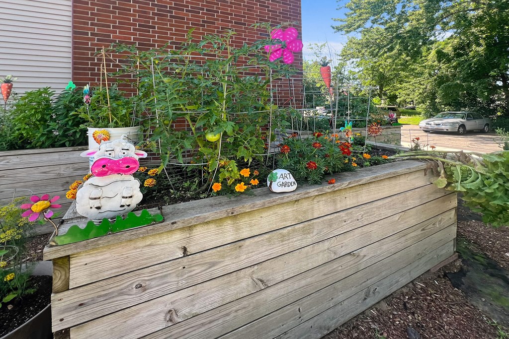 A wooden planter box with a decorative cow statue and a variety of plants.