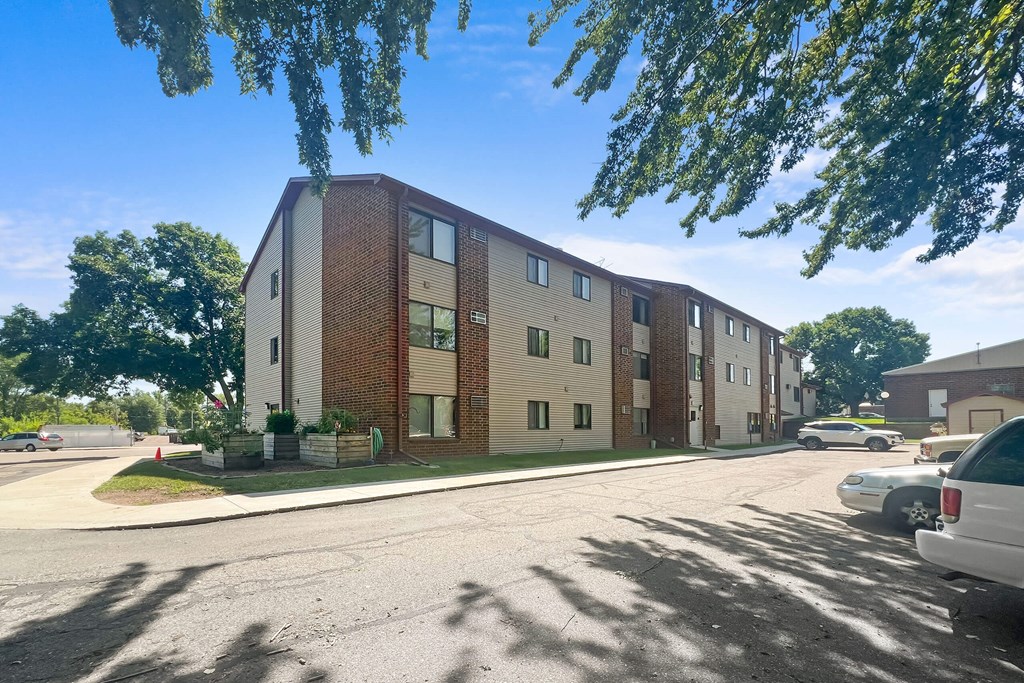 A row of apartment buildings with cars parked in front.
