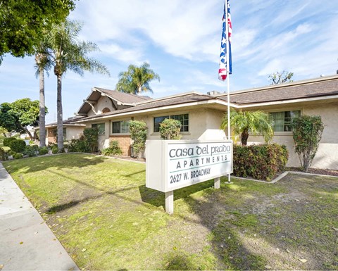 A sign for Casa Del Prado Apartments stands in front of a building.