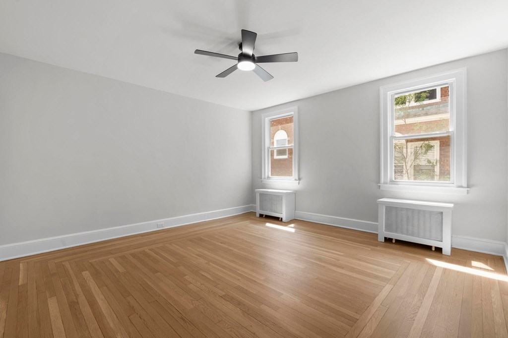 A room with a ceiling fan and two windows.