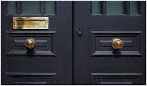 A black door with a gold handle and a mail slot.