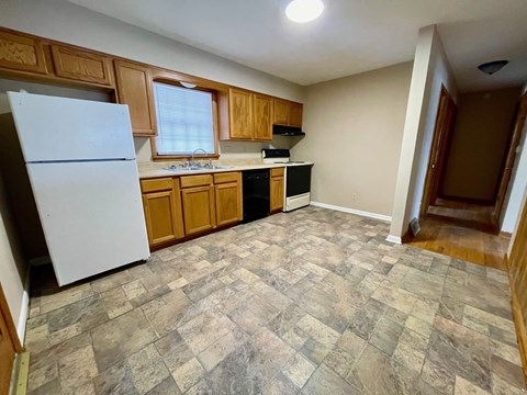 A kitchen with a white refrigerator, wooden cabinets, and a tiled floor.