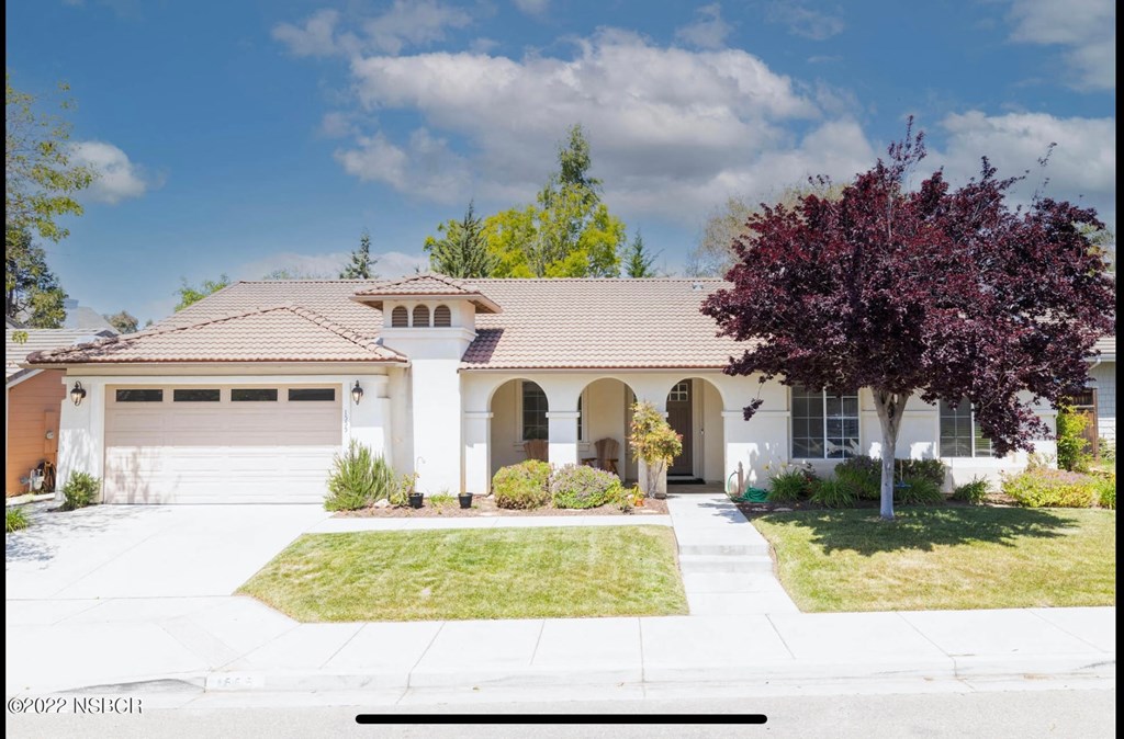 A house with a brown roof and white walls with a tree in front.