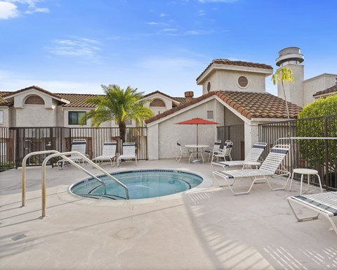 A pool with a hot tub and chairs in front of a house.