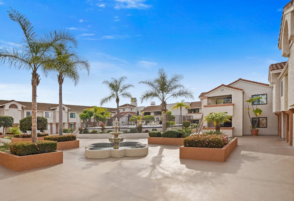 A courtyard with a fountain surrounded by palm trees and plants.