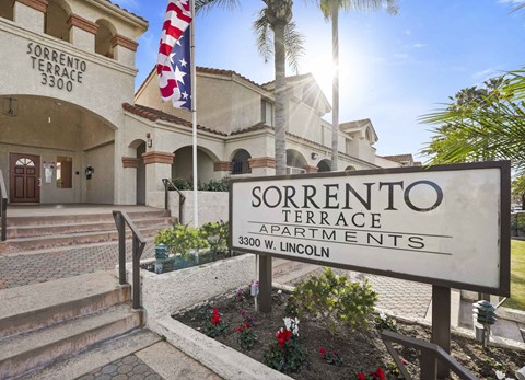 The image shows the entrance to Sorrento Terrace Apartments with a sign and a flag.