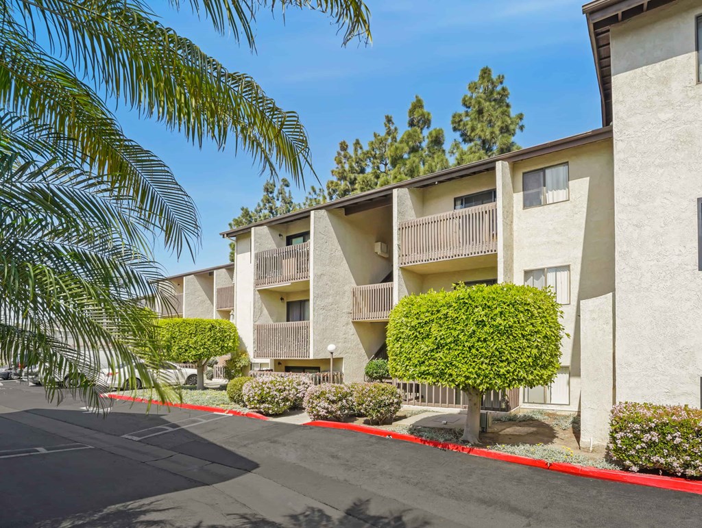 A row of apartment buildings with trees and bushes in front.