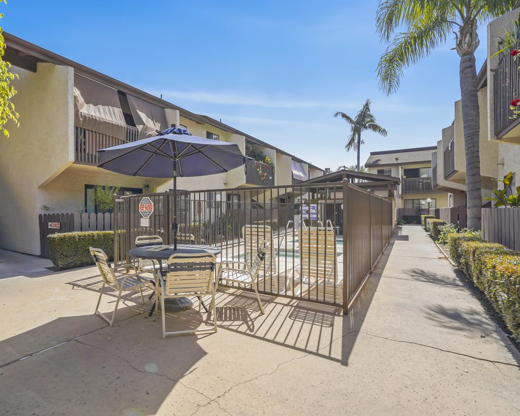 A patio with a table, chairs, and an umbrella is surrounded by a metal fence.