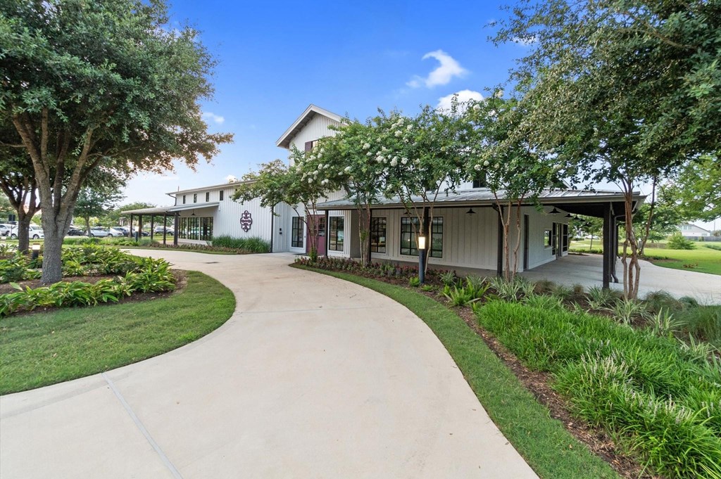 A building with a white facade and a red awning is surrounded by greenery.