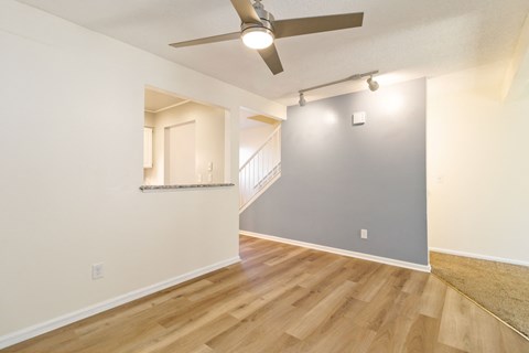 the living room and dining room of an apartment with wood floors and a ceiling fan