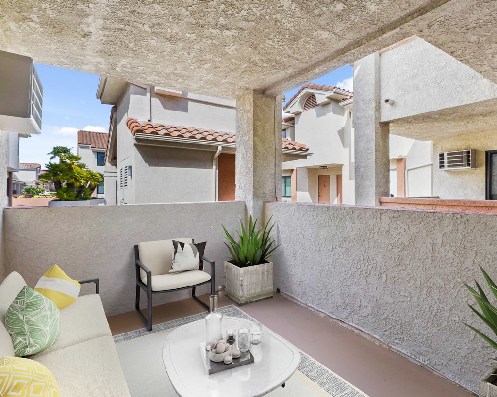 A patio with a white couch, a table with a tray, and a potted plant.