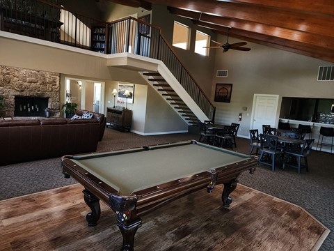 A pool table in the middle of a room with a staircase in the background.