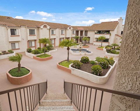 A courtyard with a fountain and flower beds in front of apartment buildings.