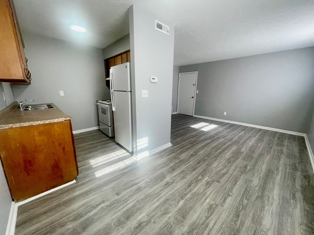 an empty living room with a kitchen and a refrigerator